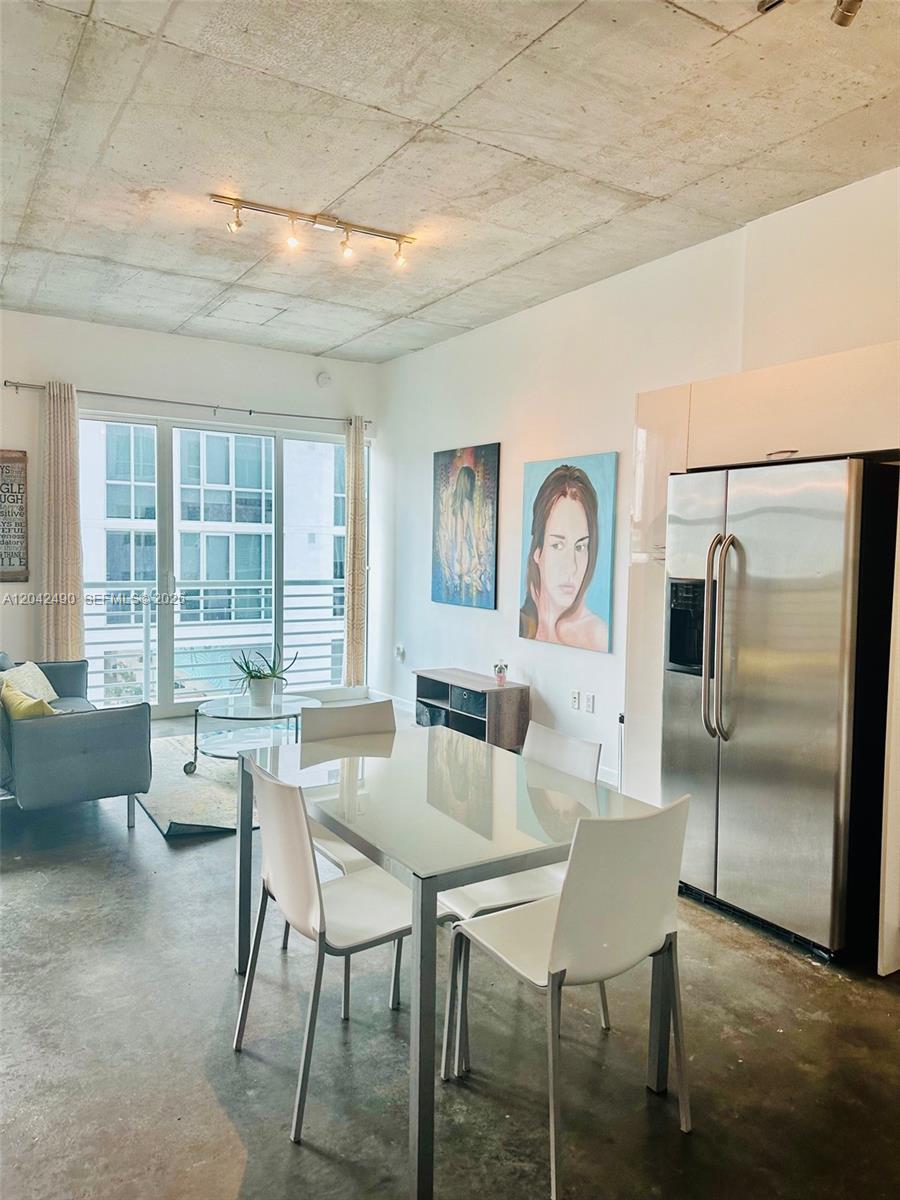 A modern apartment living and dining area features concrete ceilings, white walls, and stainless appliances — 133 NE 2 AV # 1503, Miami FL 33132, MIAMI, FL