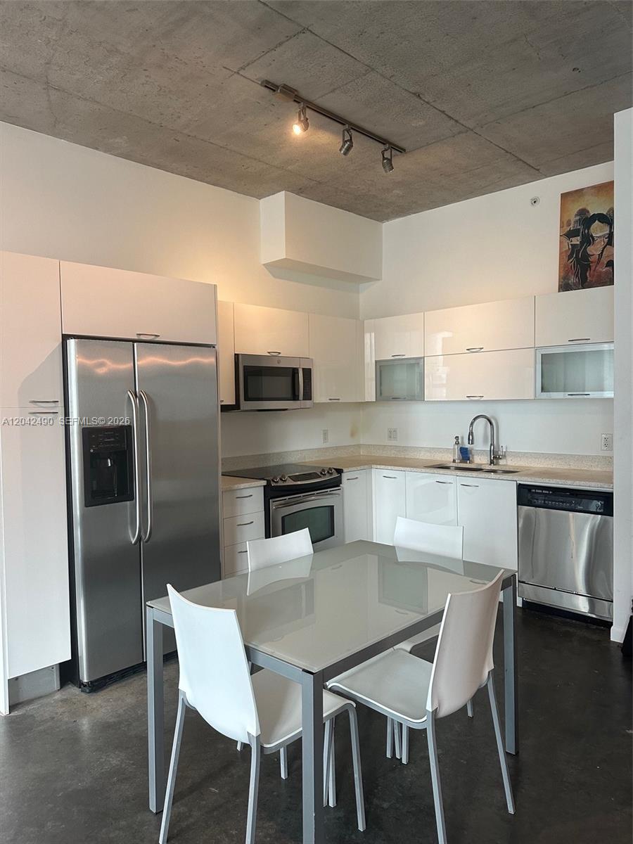 A modern kitchen features white cabinets, stainless steel appliances, and an exposed concrete ceiling — 133 NE 2 AV # 1503, Miami FL 33132, MIAMI, FL