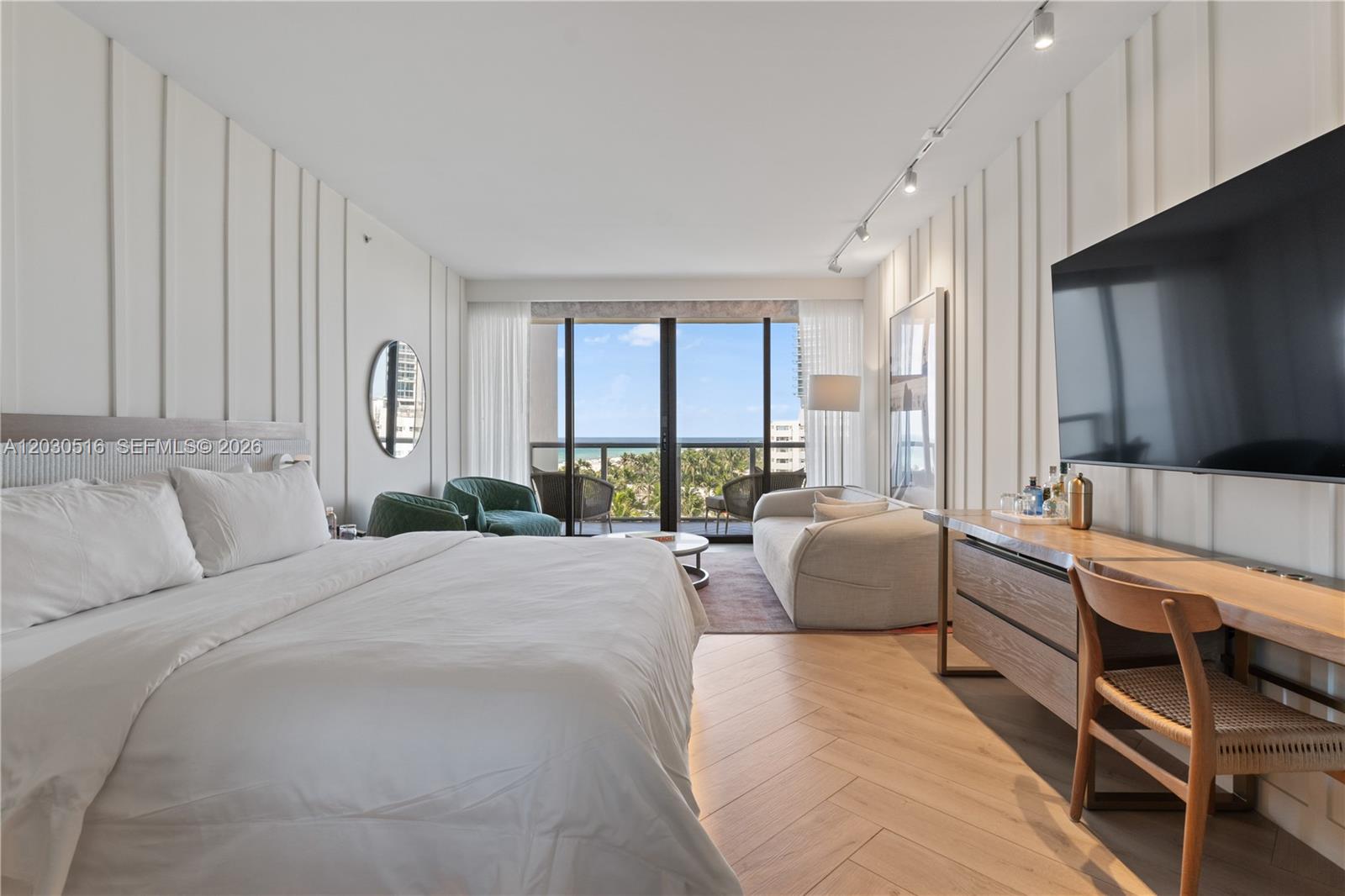 A modern bedroom features a king bed, a seating area, and a balcony with ocean views — 2201 Collins Ave # 707, Miami Beach FL 33139, MIAMI BEACH, FL