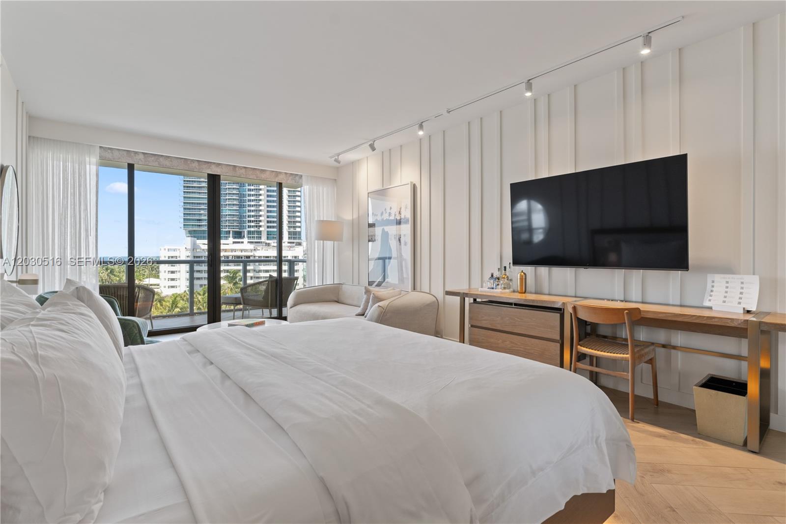 A bedroom features a bed, a wall-mounted television, a desk, and a balcony with city views — 2201 Collins Ave # 707, Miami Beach FL 33139, MIAMI BEACH, FL