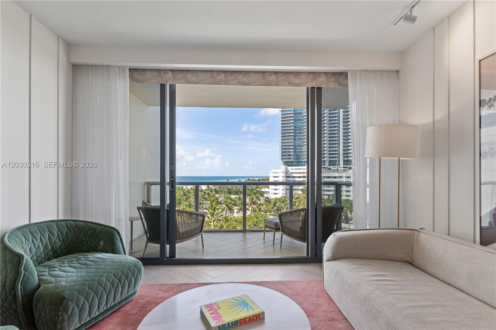 A living room features a green armchair, a beige sofa, and a balcony overlooking the ocean — 2201 Collins Ave # 707, Miami Beach FL 33139, MIAMI BEACH, FL