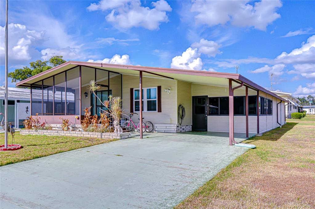 A single-story manufactured home with a screened-in porch, carport, and light-colored siding — 35827 BRISA DRIVE, ZEPHYRHILLS, FL
