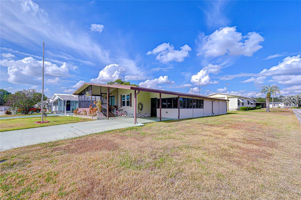 A single-story manufactured home with a carport, screened porch, and a large grassy yard — 35827 BRISA DRIVE, ZEPHYRHILLS, FL