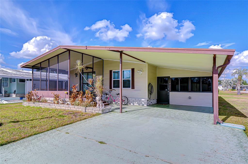 A single-story manufactured home features a screened-in porch, a carport, and a concrete driveway — 35827 BRISA DRIVE, ZEPHYRHILLS, FL