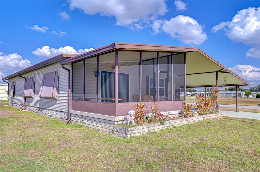 A mobile home with a screened-in porch and a covered carport under a blue sky — 35827 BRISA DRIVE, ZEPHYRHILLS, FL