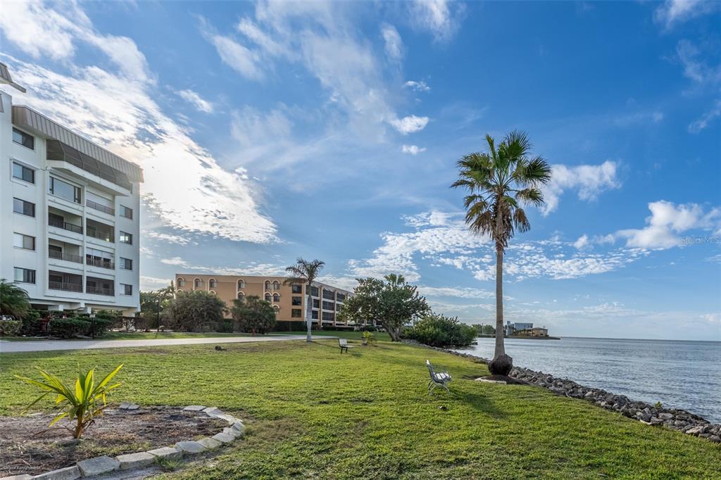 A grassy waterfront lawn features palm trees, benches, and a multi-story apartment building — 1477 PARK BEACH CIRCLE UNIT 11, PUNTA GORDA, FL