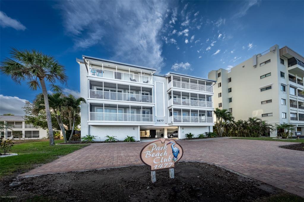 A three-story apartment building with screened balconies stands behind a sign in a paved lot — 1477 PARK BEACH CIRCLE UNIT 11, PUNTA GORDA, FL