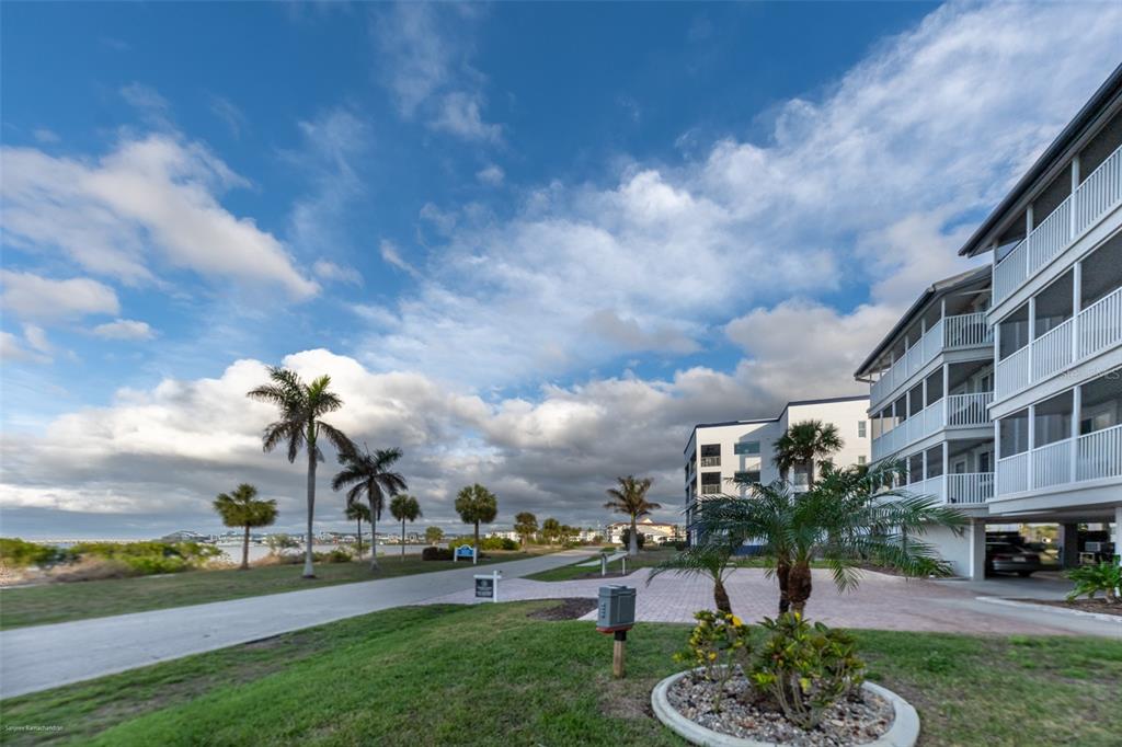 Exterior view of a multi-story apartment building with balconies, palm trees, and a paved driveway — 1477 PARK BEACH CIRCLE UNIT 11, PUNTA GORDA, FL