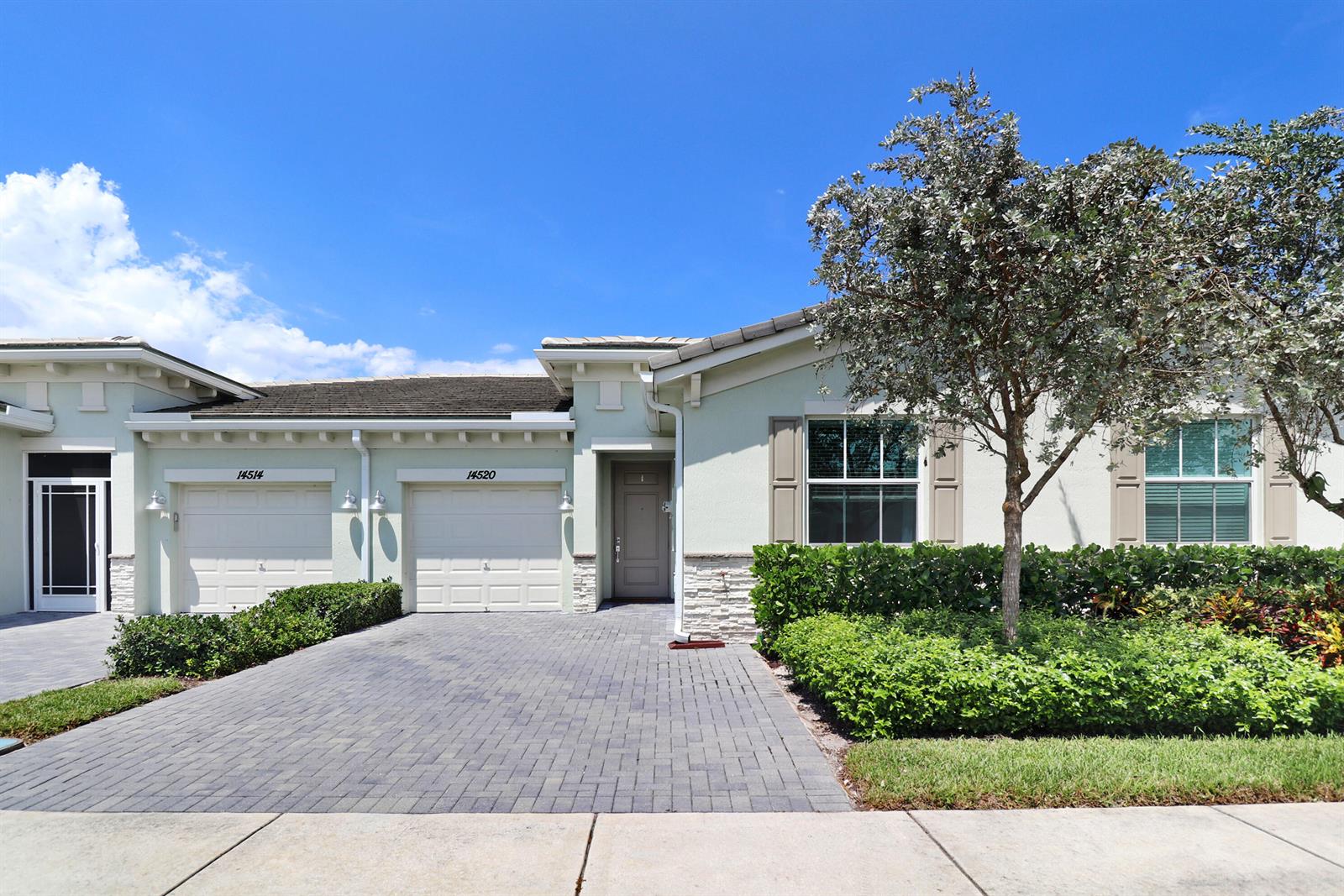 A light-colored residential building features two garage doors, a front entrance, and landscaped greenery — 14520 Wiley Range Road, Delray Beach FL 33446, DELRAY BEACH, FL