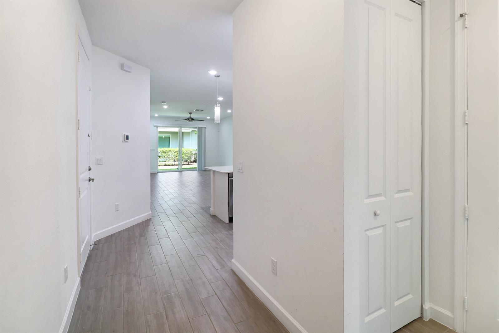 A hallway with gray wood-look tile flooring leads toward an open-concept kitchen and living area — 14520 Wiley Range Road, Delray Beach FL 33446, DELRAY BEACH, FL
