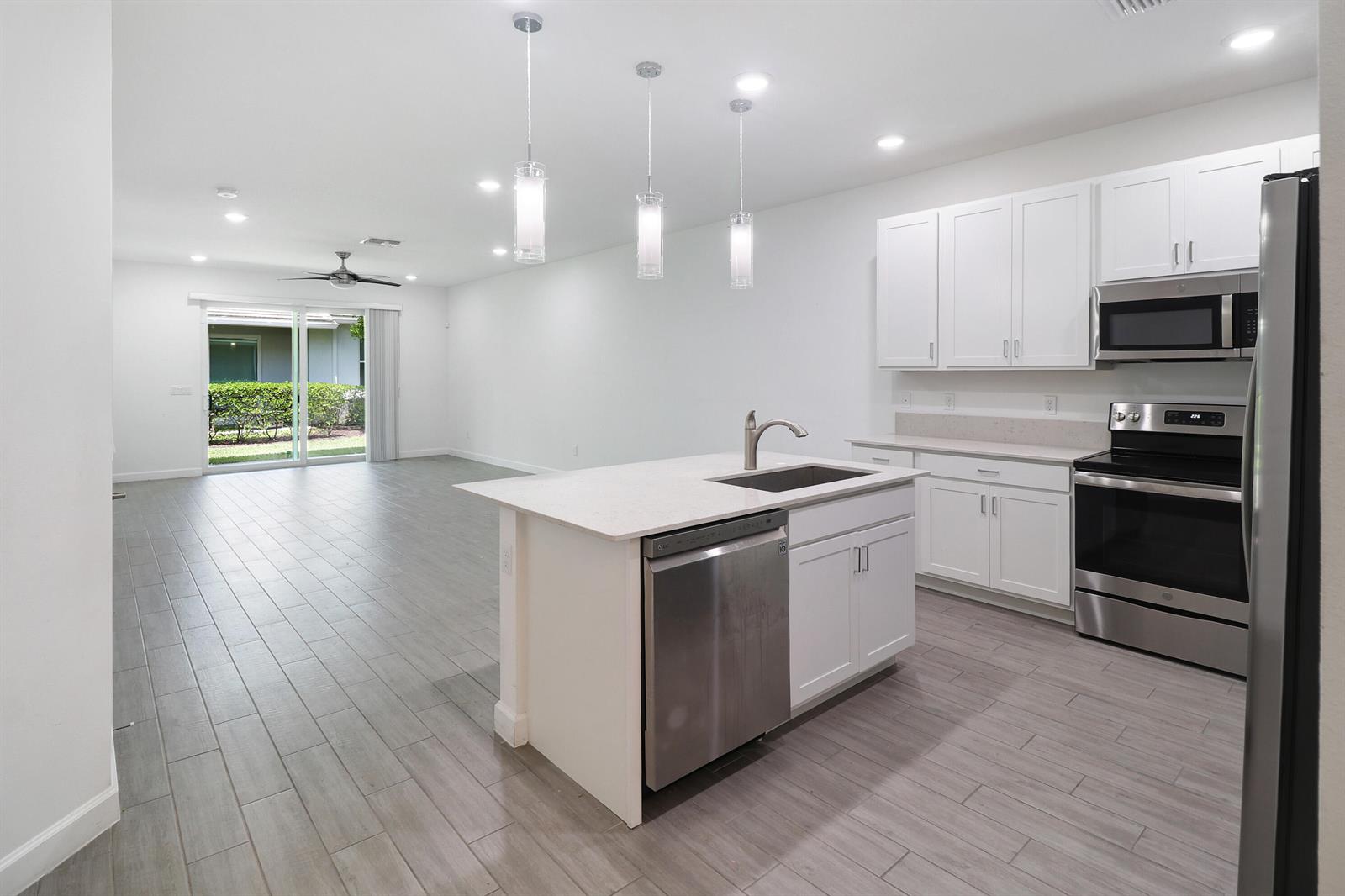 A modern kitchen with white cabinets, stainless steel appliances, and an island overlooks an open room — 14520 Wiley Range Road, Delray Beach FL 33446, DELRAY BEACH, FL