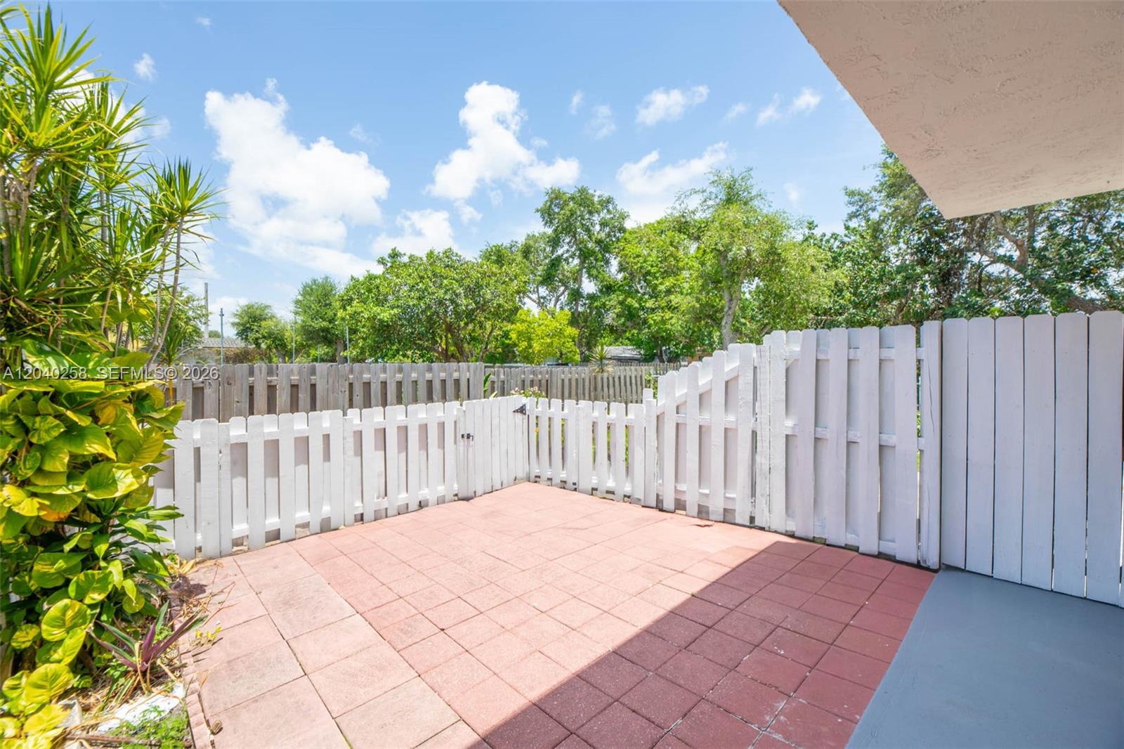 A paved patio area is enclosed by a white picket fence and a wooden privacy fence — 1450 NE 151st St # 101, Miami FL 33162, MIAMI, FL
