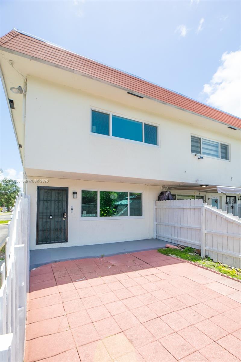 A two-story building exterior features a paved patio, a white fence, and a front door — 1450 NE 151st St # 101, Miami FL 33162, MIAMI, FL