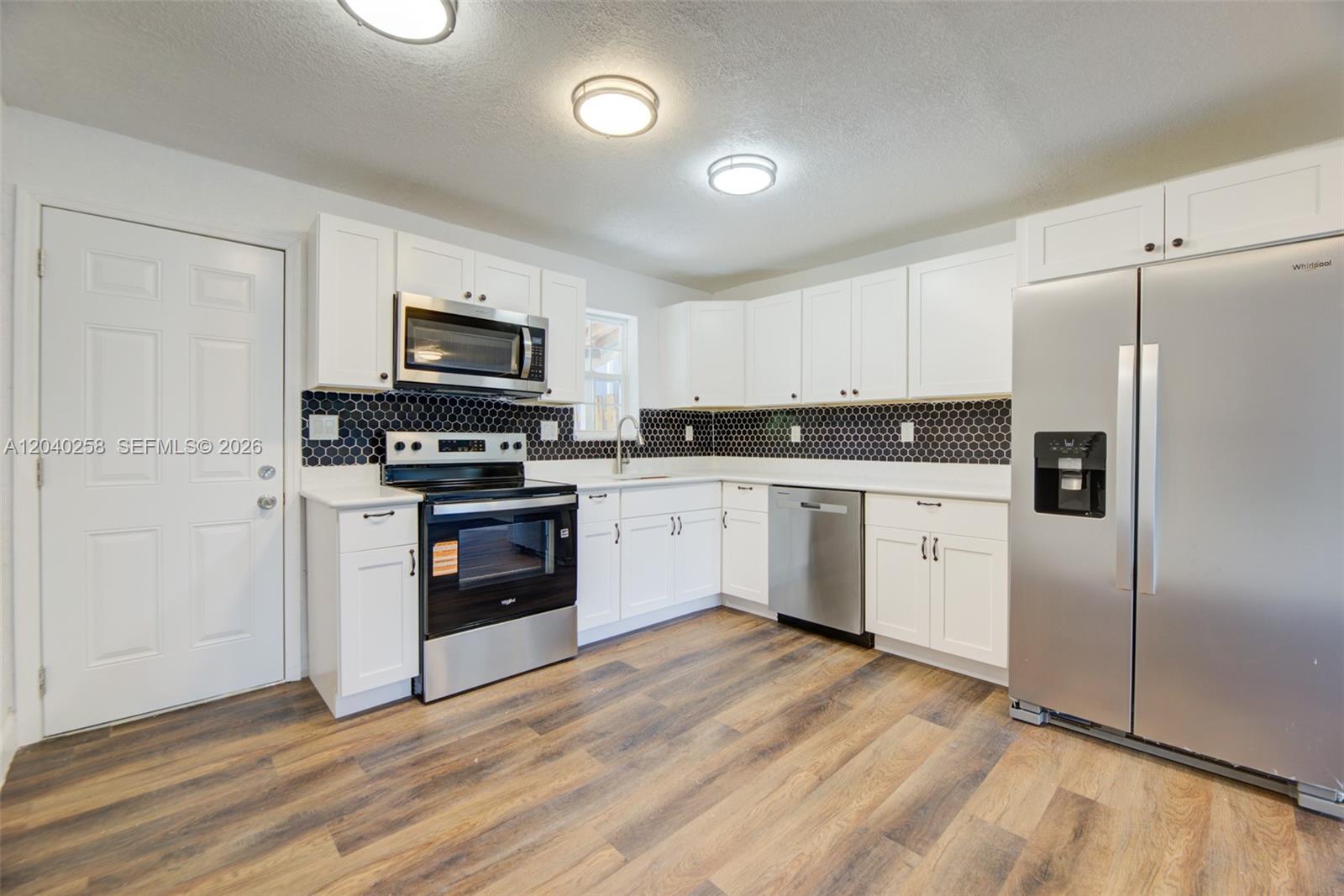 A kitchen features white cabinets, stainless steel appliances, and a black hexagonal tile backsplash — 1450 NE 151st St # 101, Miami FL 33162, MIAMI, FL