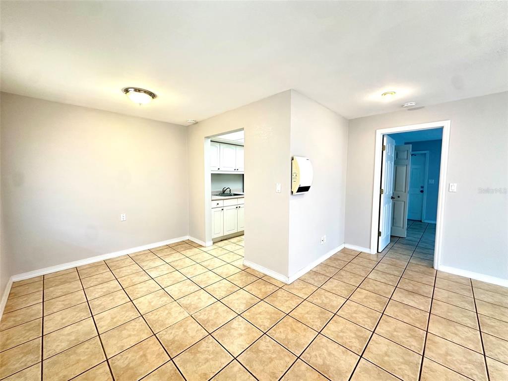 A dining area with beige tile flooring leads into a kitchen through an open doorway — 1458 CLEVELAND STREET, CLEARWATER, FL
