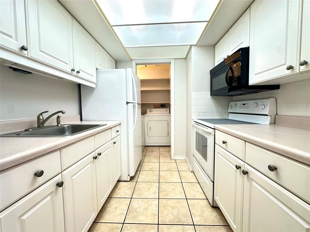 A galley kitchen features white cabinets, light countertops, tile flooring, and a laundry closet — 1458 CLEVELAND STREET, CLEARWATER, FL