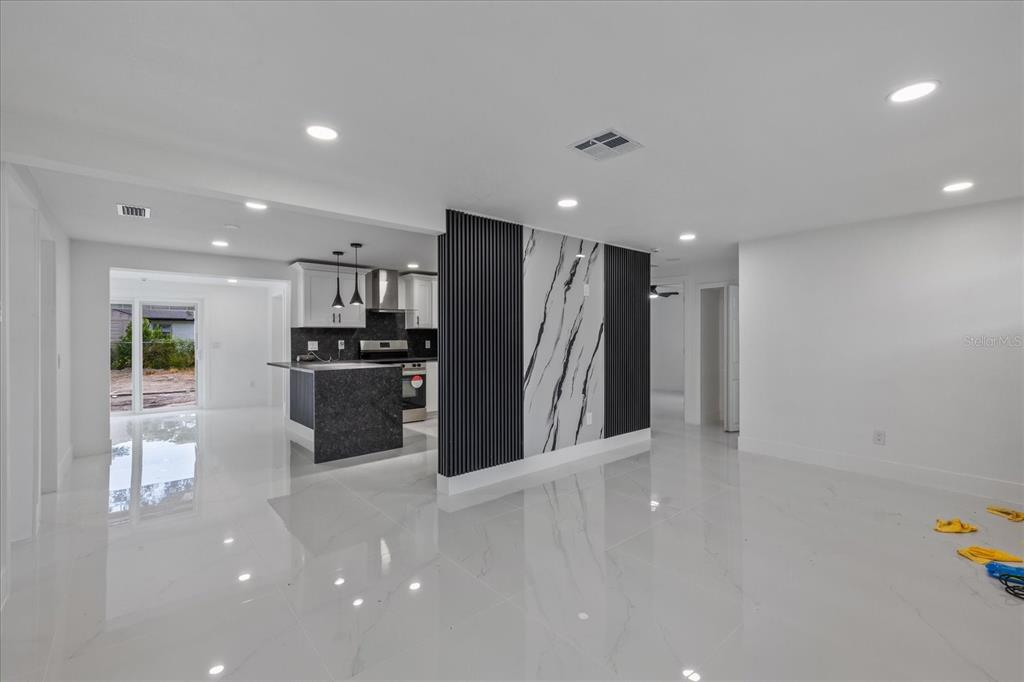 A modern open-concept living area features white tile floors and a black-and-white marble accent wall — 4853 ROSEDALE LANE, HOLIDAY, FL