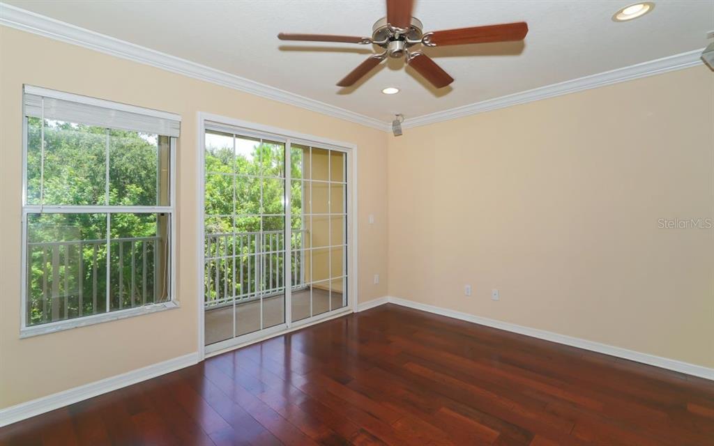 A bedroom with hardwood floors, a ceiling fan, and sliding glass doors leading to a balcony — 7339 BLACK WALNUT WAY, LAKEWOOD RANCH, FL