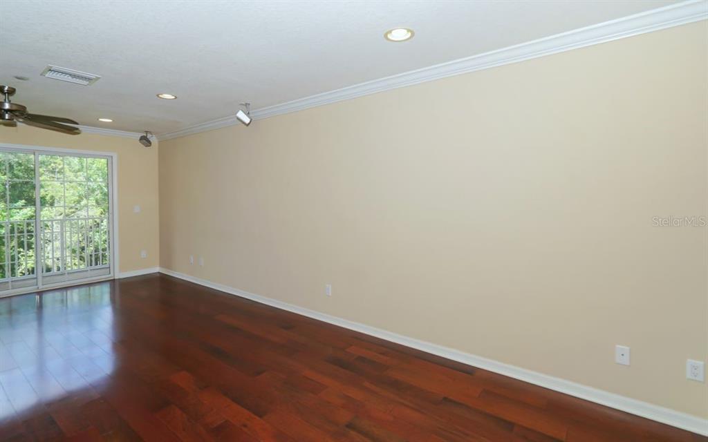 A spacious room with dark hardwood floors, beige walls, and a sliding glass door — 7339 BLACK WALNUT WAY, LAKEWOOD RANCH, FL