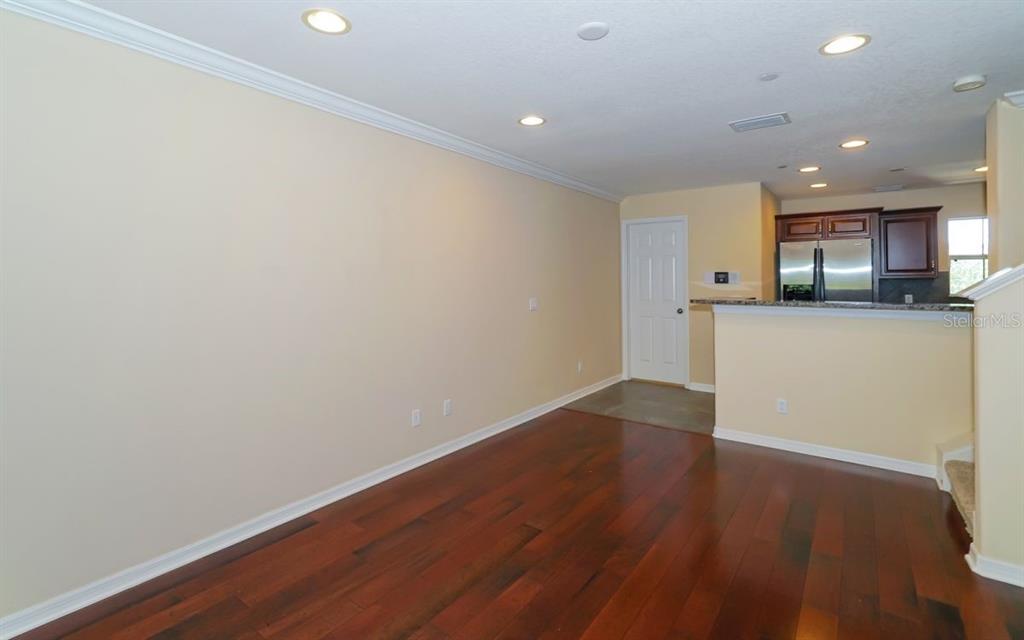 An empty living room with hardwood floors, recessed lighting, and an open kitchen with dark cabinets — 7339 BLACK WALNUT WAY, LAKEWOOD RANCH, FL