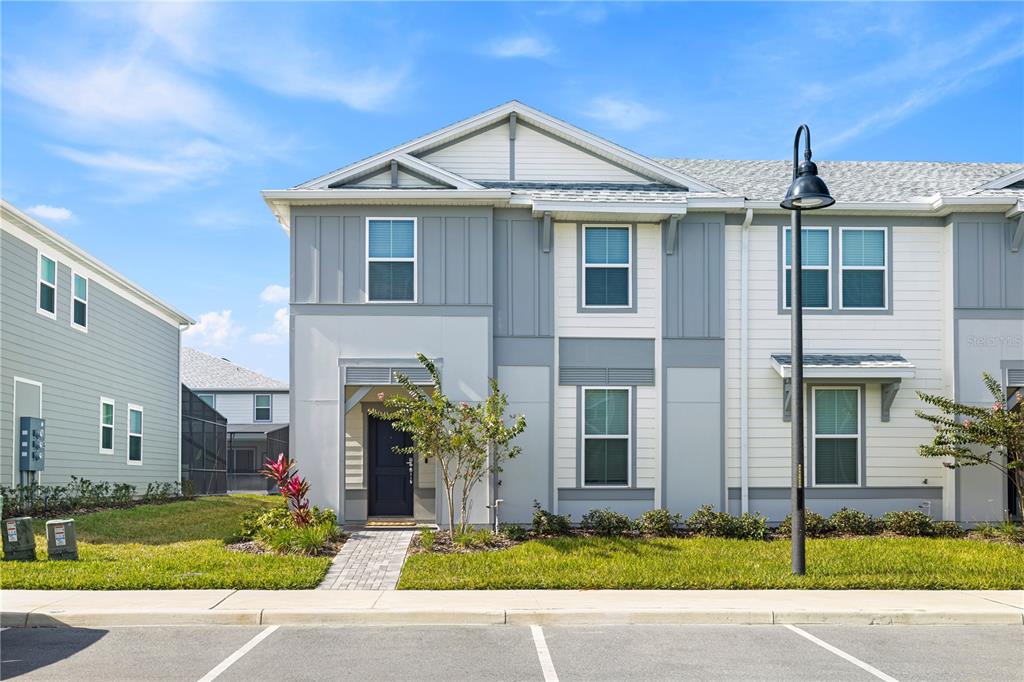 A two-story townhouse exterior features gray and white siding with a paved walkway — 1277 BLUE ISLAND DRIVE, CLERMONT, FL