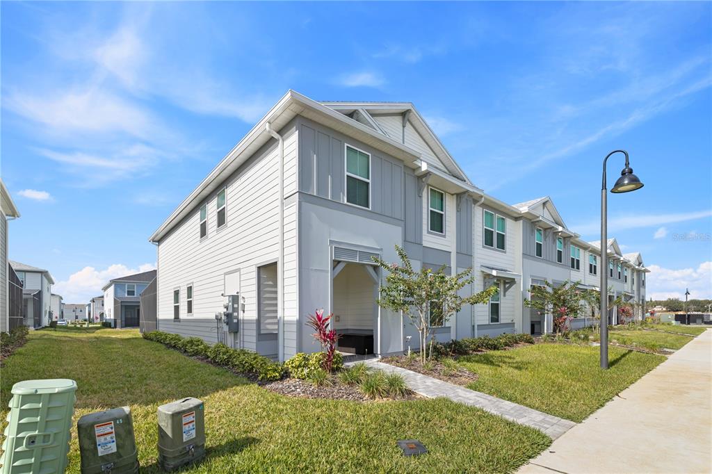 A two-story townhouse exterior with gray siding, a covered entryway, and a paved walkway — 1277 BLUE ISLAND DRIVE, CLERMONT, FL