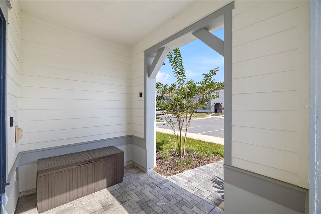 A covered porch features white horizontal siding, a gray storage bin, and a brick floor — 1277 BLUE ISLAND DRIVE, CLERMONT, FL