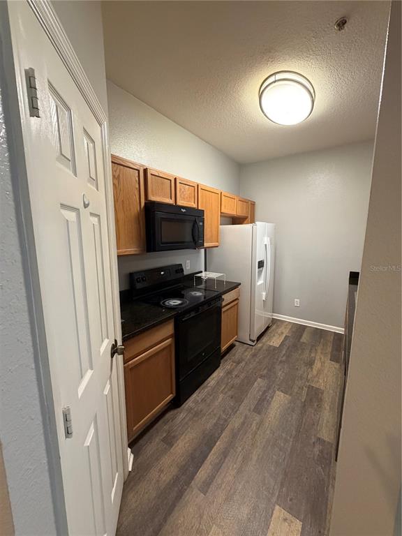 A galley kitchen features wood cabinets, black appliances, and wood-look flooring — 6100 STEVENSON DRIVE UNIT 207, ORLANDO, FL