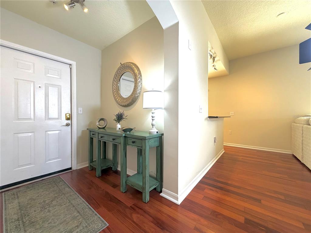 A foyer features a teal console table, a round mirror, and hardwood flooring — 909 WATERSIDE LANE UNIT 205, CELEBRATION, FL
