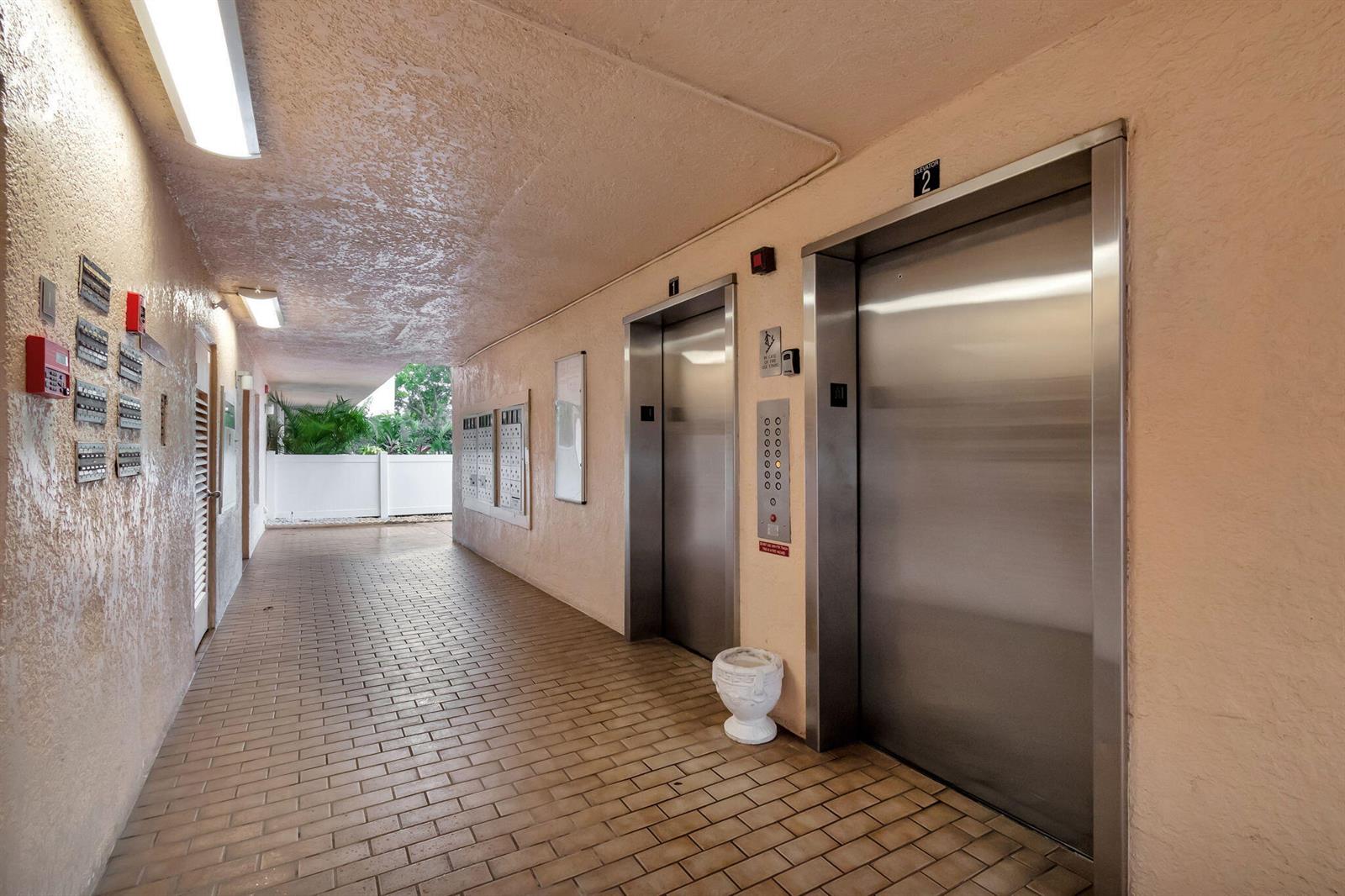 A hallway with brick flooring features two stainless steel elevators and a wall of mailboxes — 14575 Bonaire Boulevard # 402, Delray Beach FL 33446, DELRAY BEACH, FL