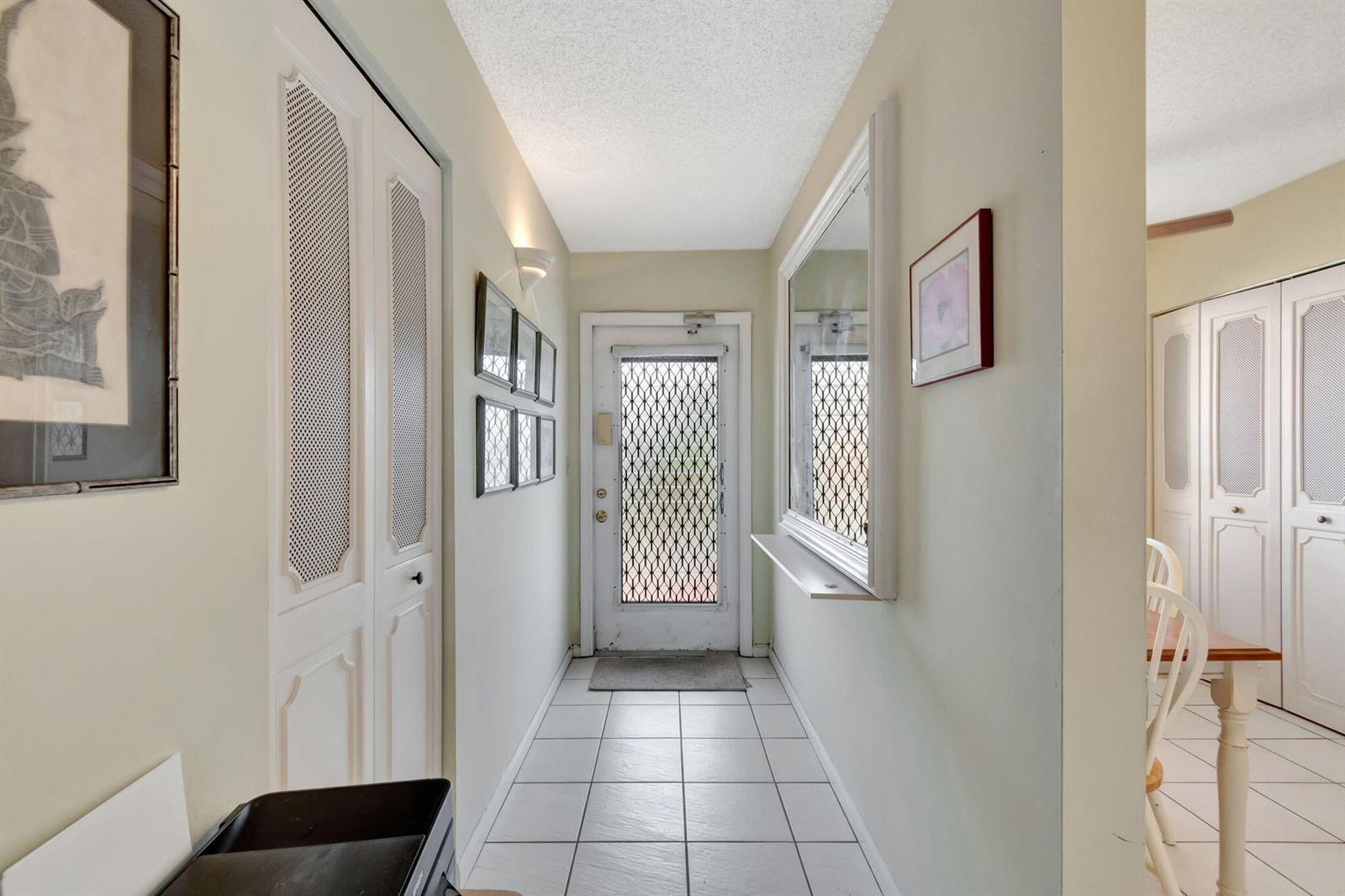 A tiled entryway features white louvered closet doors, a security screen door, and wall art — 14575 Bonaire Boulevard # 402, Delray Beach FL 33446, DELRAY BEACH, FL