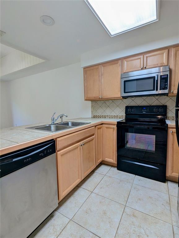 A kitchen features light wood cabinets, stainless steel appliances, tile countertops, and a tiled floor — 6125 TOPHER TRAIL UNIT 62A, MULBERRY, FL