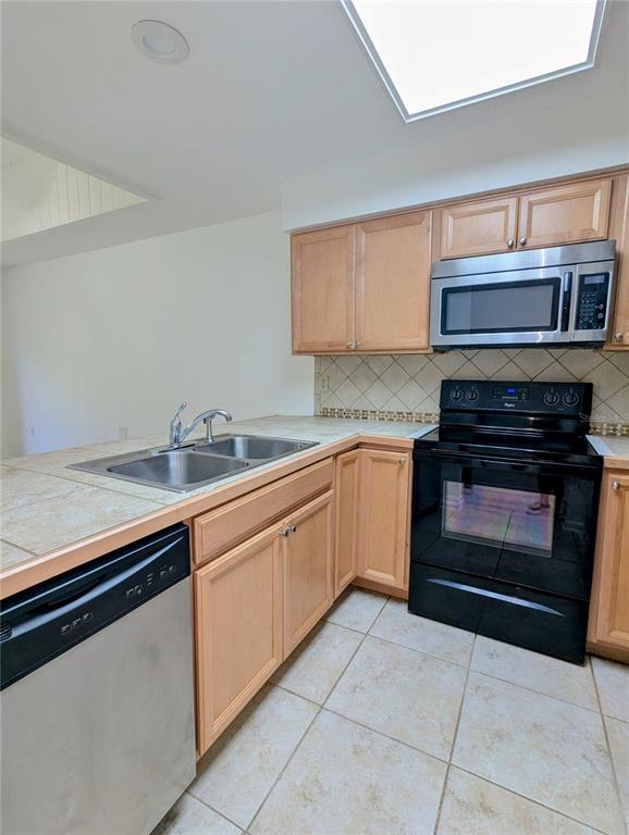 A kitchen features light wood cabinets, stainless steel appliances, tile countertops, and a tiled floor — 6125 TOPHER TRAIL UNIT 62A, MULBERRY, FL