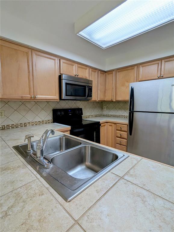 A kitchen features light wood cabinets, stainless steel appliances, and tiled countertops with a sink — 6125 TOPHER TRAIL UNIT 62A, MULBERRY, FL