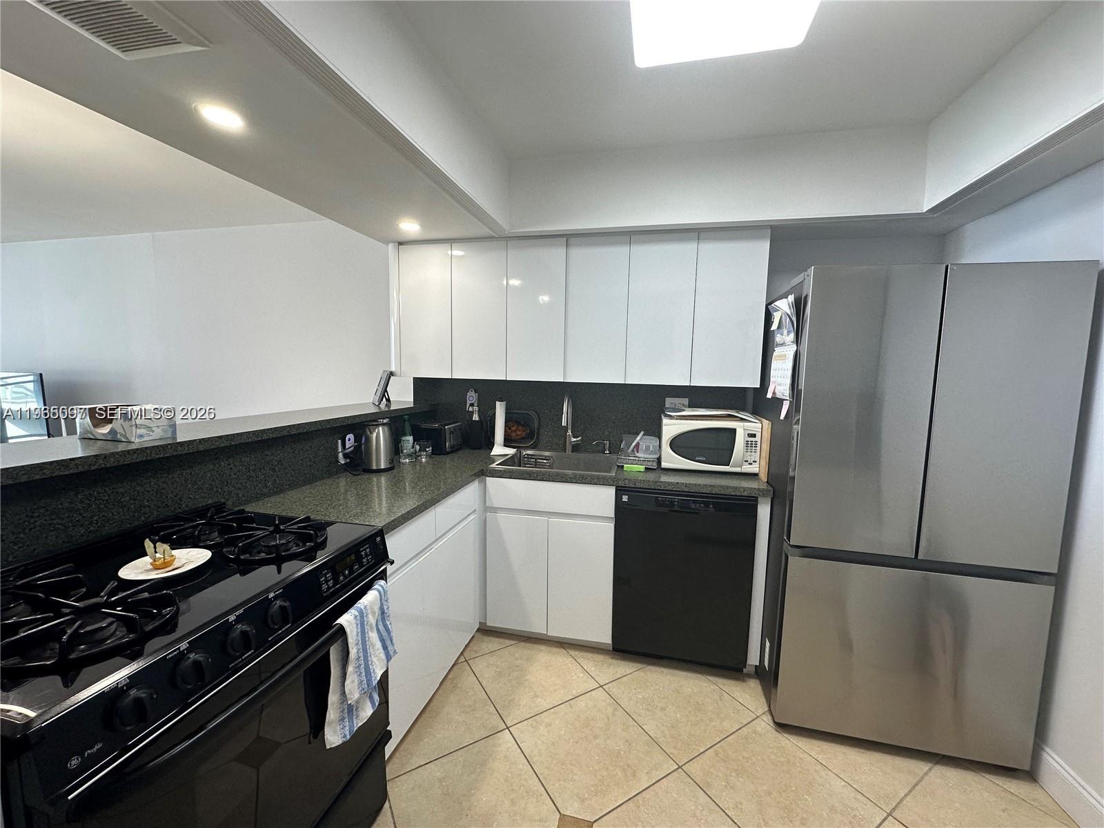 A kitchen features white cabinets, black appliances, dark countertops, and light-colored tile flooring — 2030 S Ocean Dr # 2217, Hallandale Beach FL 33009, HALLANDALE BEACH, FL