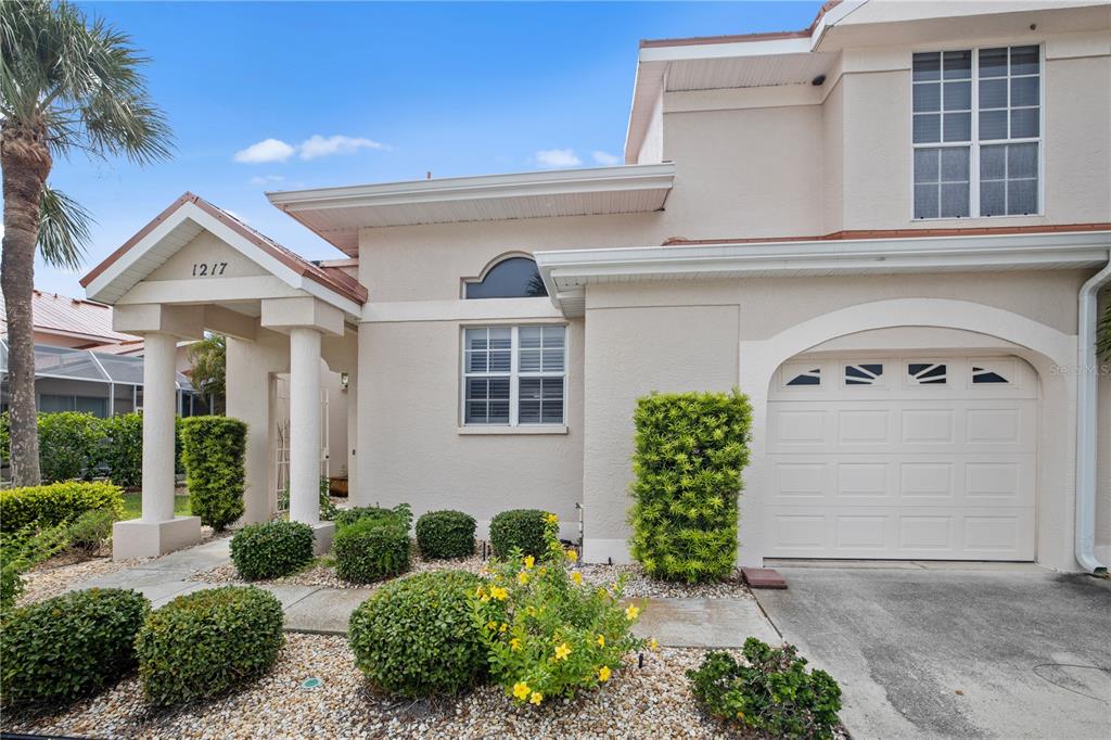A two-story stucco house exterior features a covered entryway, a garage, and landscaped bushes — 1217 GORDA CAY LANE, PUNTA GORDA, FL
