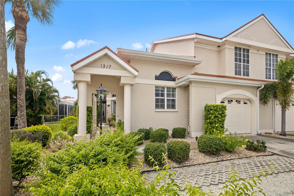 A two-story stucco townhouse features a covered entryway, a garage, and landscaped front yard — 1217 GORDA CAY LANE, PUNTA GORDA, FL