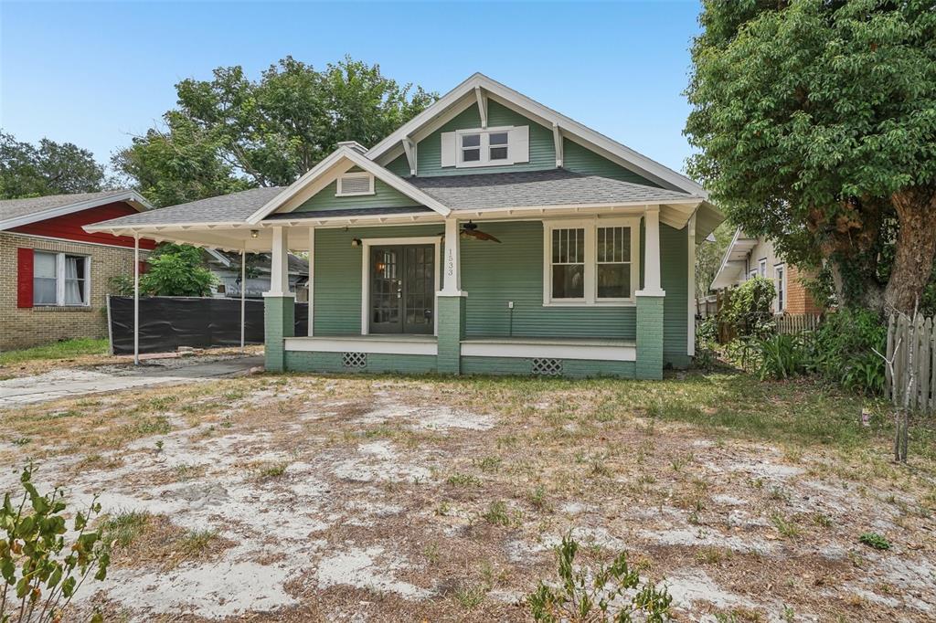 A green bungalow with a front porch, carport, and a large, sandy front yard — 1533 E ELM ROAD, LAKELAND, FL