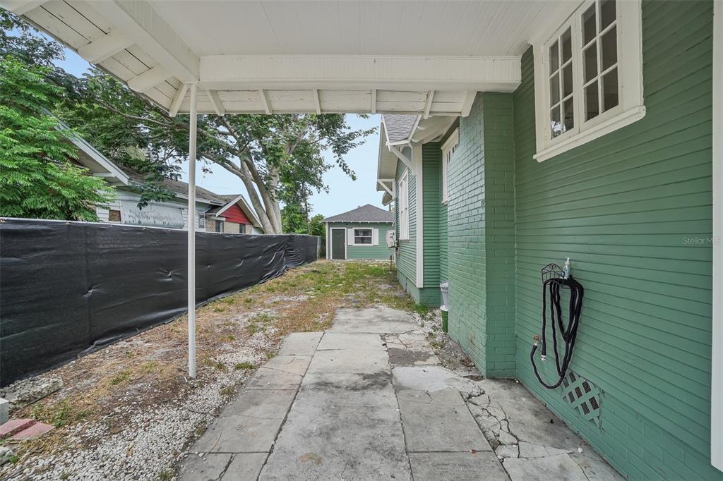 A covered concrete patio sits beside a green house with a detached garage in back — 1533 E ELM ROAD, LAKELAND, FL