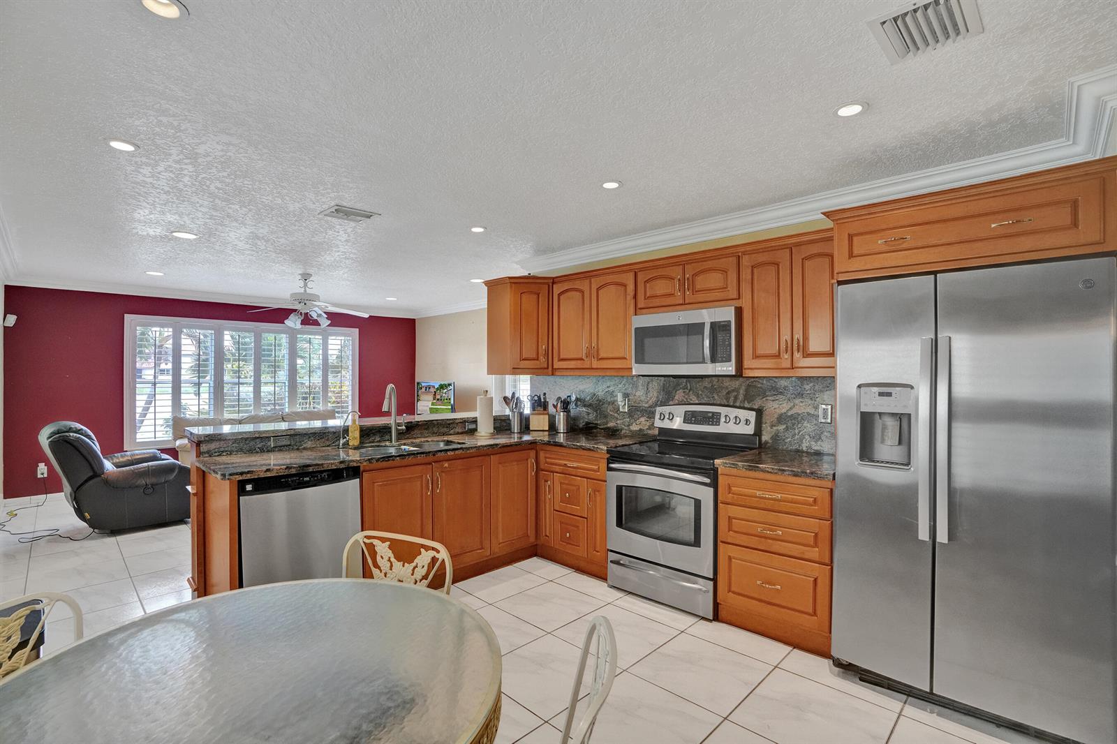 A kitchen with wood cabinets, stainless steel appliances, and granite countertops opens to a living area — 18144 SW 20th Street, Miramar FL 33029, MIRAMAR, FL