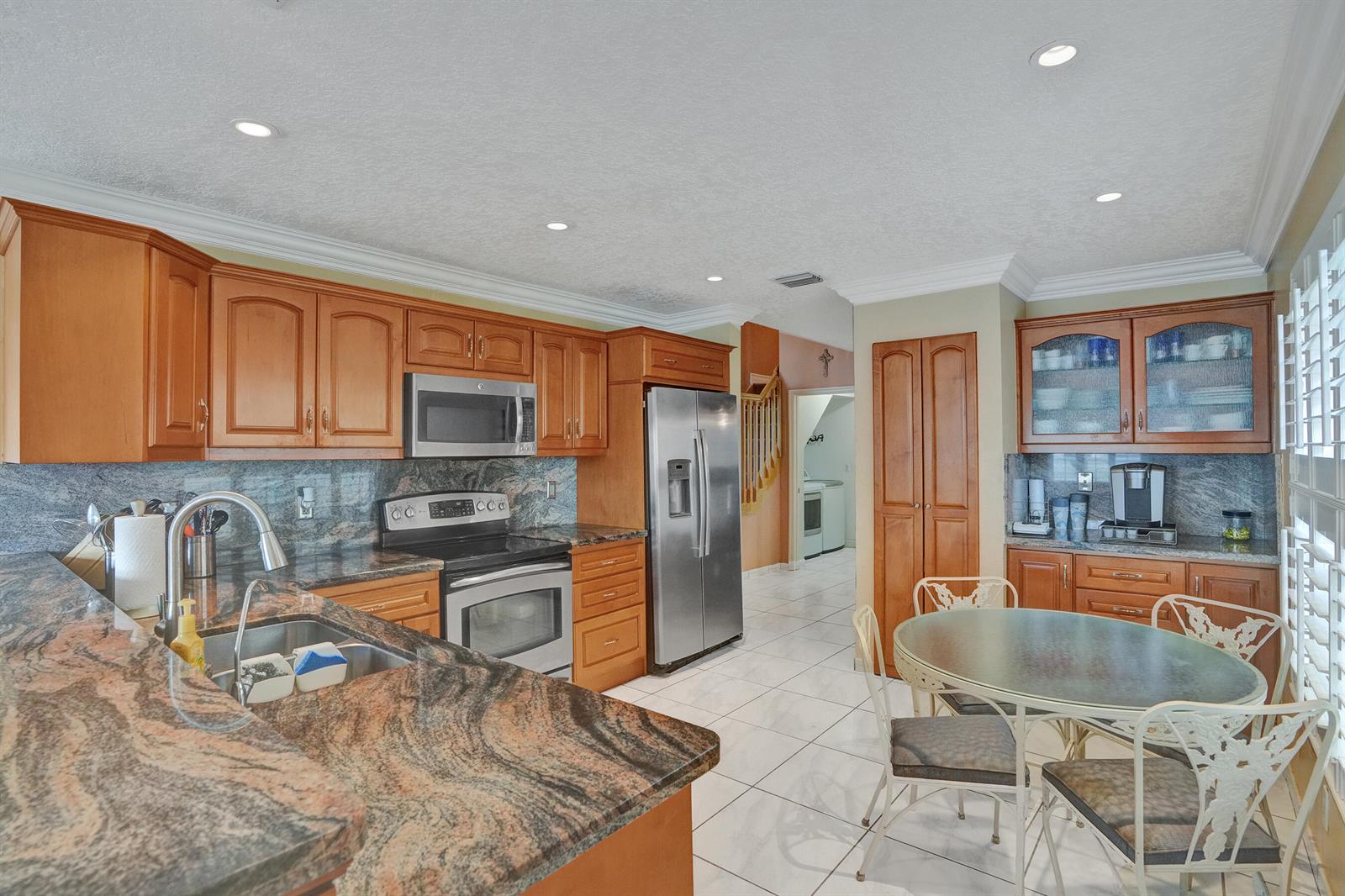 A kitchen with wood cabinets, granite countertops, stainless steel appliances, and a small dining table — 18144 SW 20th Street, Miramar FL 33029, MIRAMAR, FL