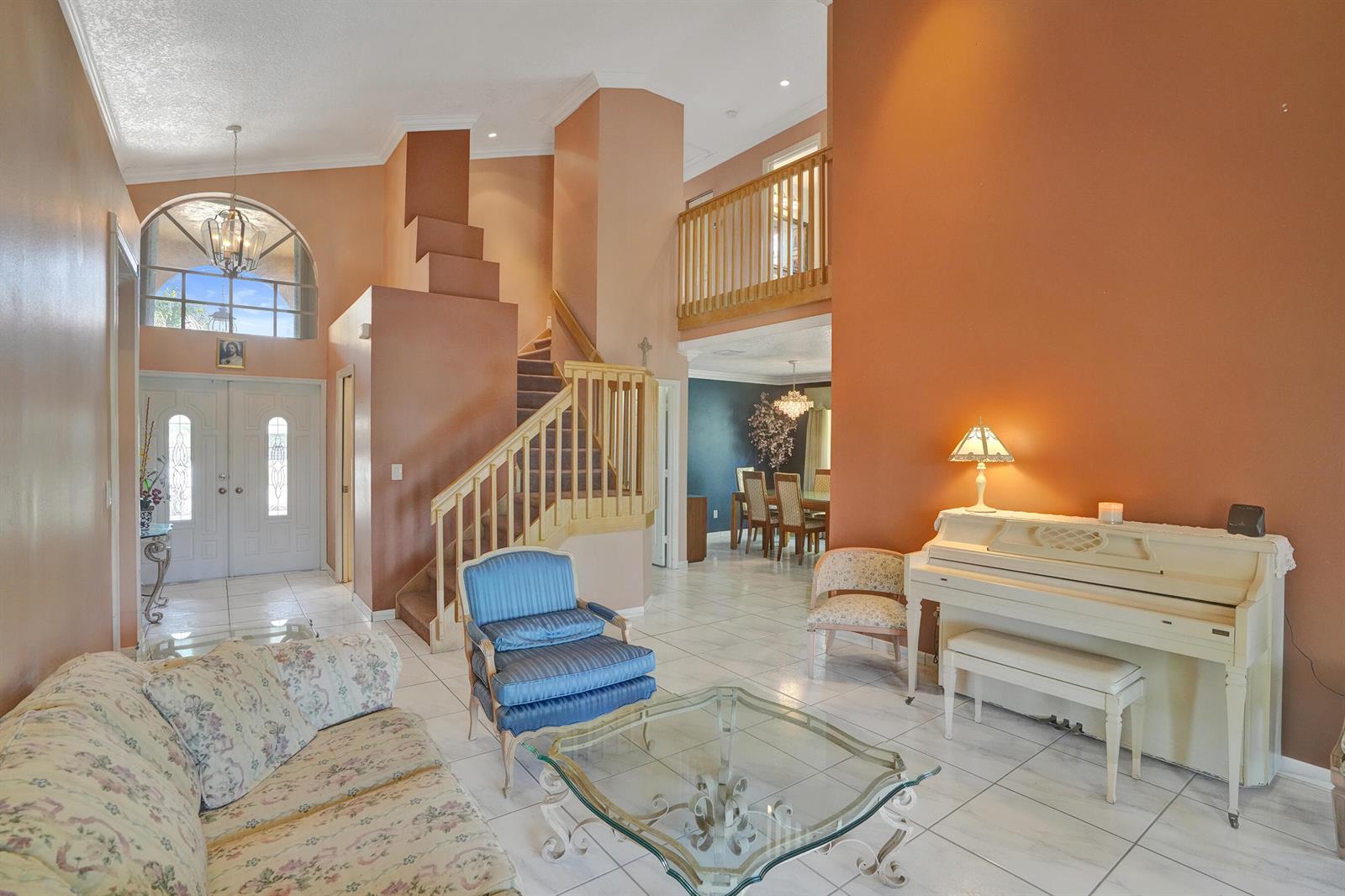 A living room features a staircase, a white piano, and a floral sofa on tile floors — 18144 SW 20th Street, Miramar FL 33029, MIRAMAR, FL