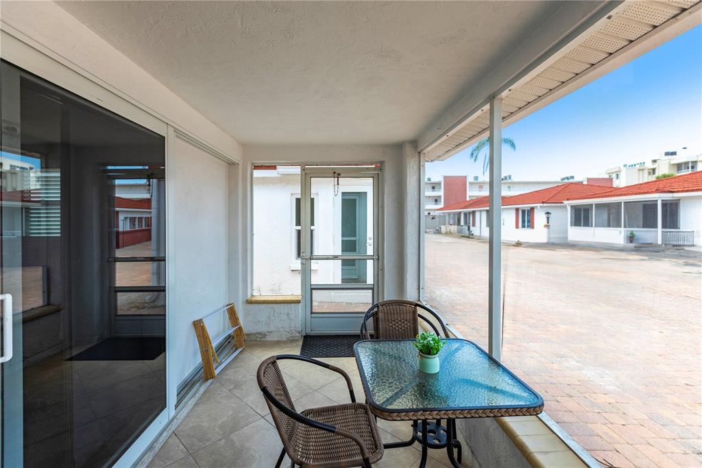 A screened-in patio features tile flooring, a small glass table, and chairs overlooking a courtyard — 6154 MIDNIGHT PASS ROAD UNIT D15, SARASOTA, FL