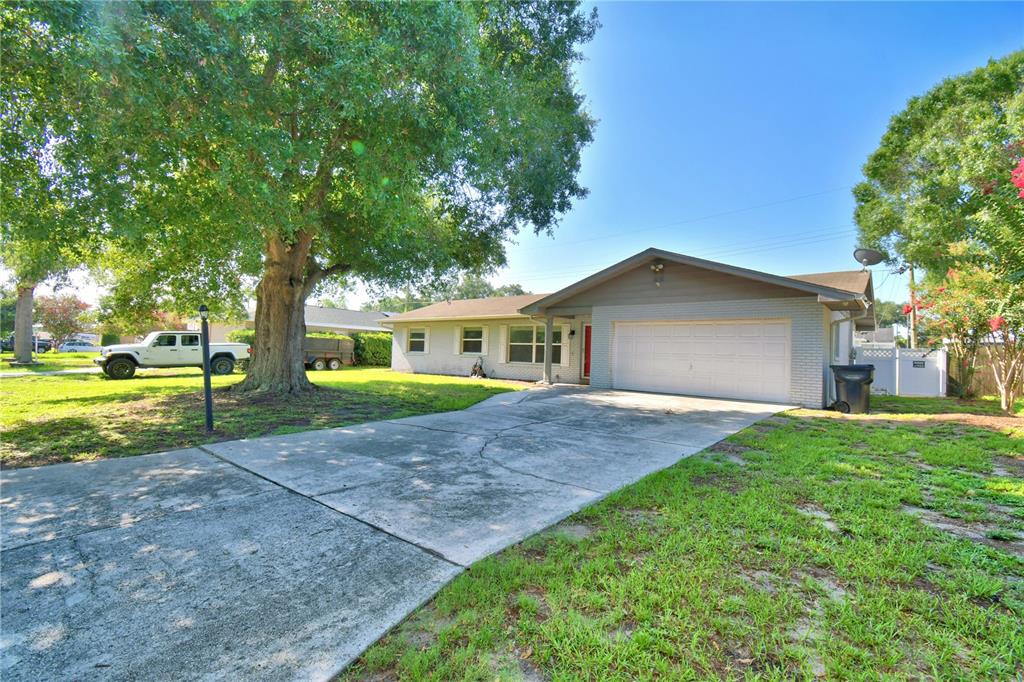 A single-story house with a white brick facade, a two-car garage, and a large tree — 153 BROWNING CIRCLE, WINTER HAVEN, FL