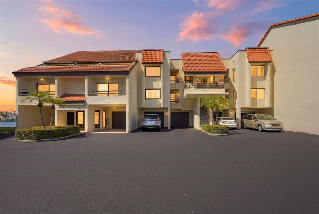 A multi-story residential building with a tiled roof, parking bays, and palm trees — 128 1ST STREET E. UNIT 102, TIERRA VERDE, FL