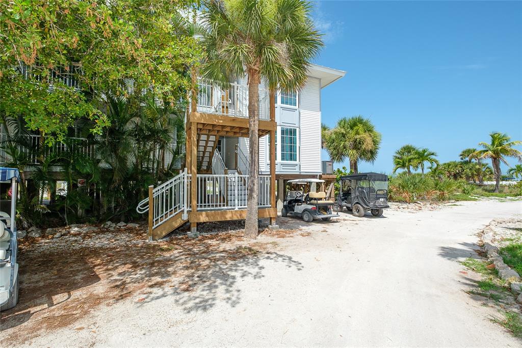 An elevated house with a wooden staircase and golf carts parked underneath on a sandy lot — 7462 PALM ISLAND DRIVE UNIT 3113, PLACIDA, FL