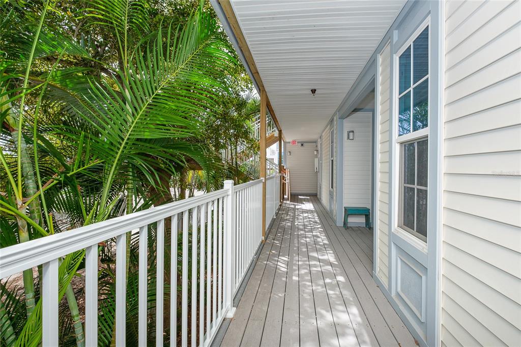 An outdoor wooden walkway with a white railing overlooks palm trees beside a building exterior — 7462 PALM ISLAND DRIVE UNIT 3113, PLACIDA, FL