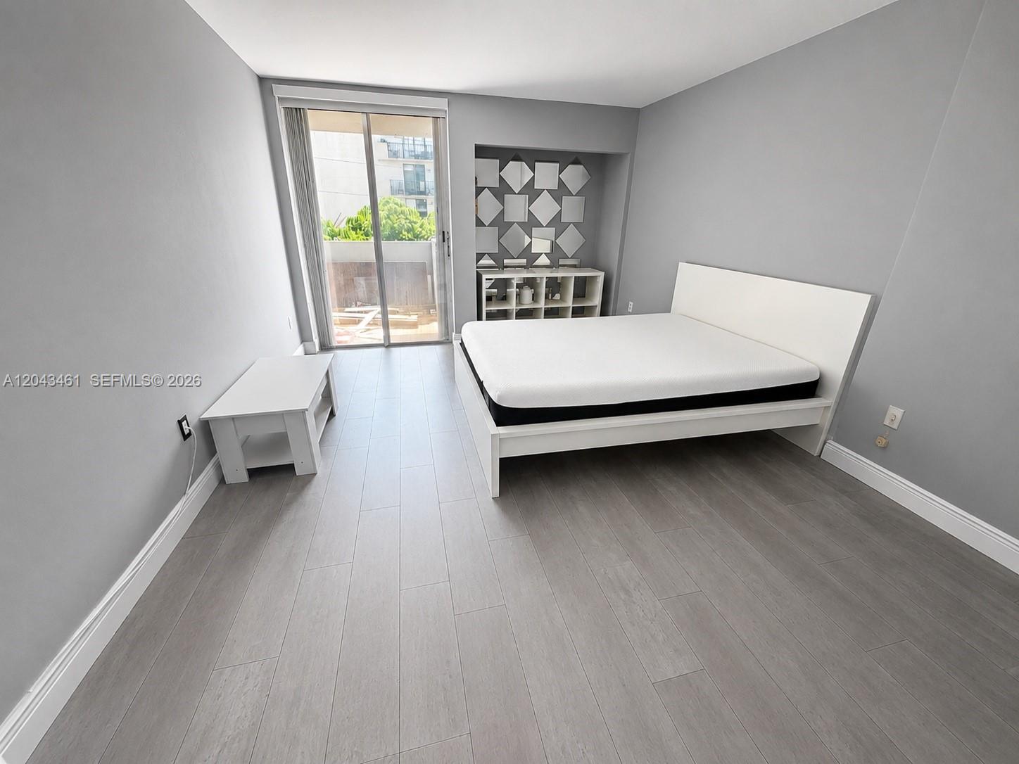 A bedroom features gray walls, light wood-look flooring, a white bed frame, and a sliding door — 1670 Bay Rd # 3D, Miami Beach FL 33139, MIAMI BEACH, FL