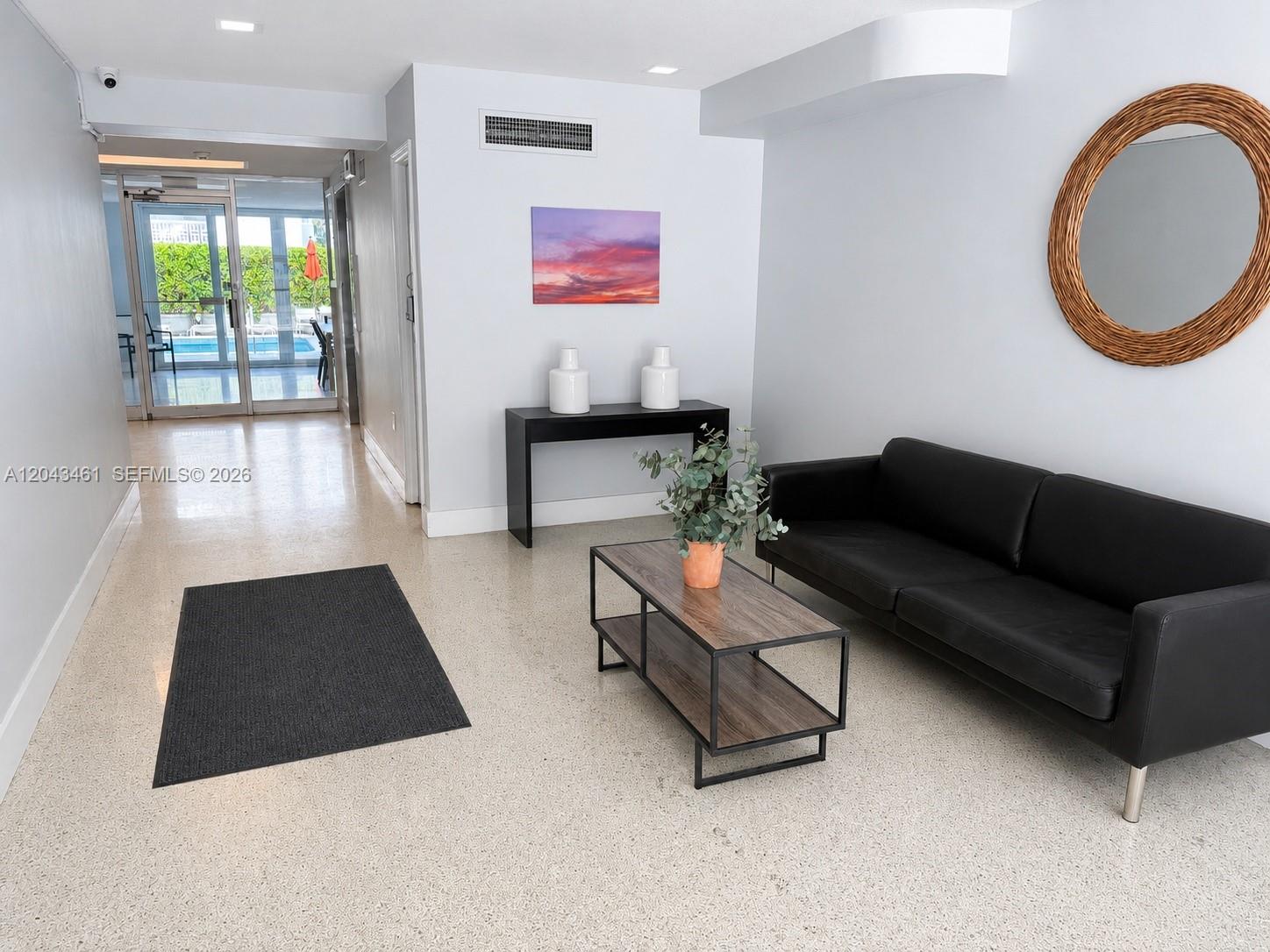 A modern lobby features a black sofa, a coffee table, and a view of a pool — 1670 Bay Rd # 3D, Miami Beach FL 33139, MIAMI BEACH, FL