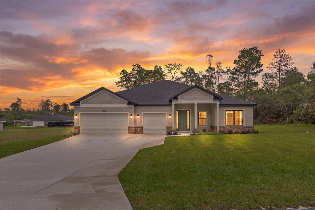 A single-story house with a three-car garage and a concrete driveway at sunset — 8065 N DOTHAN DRIVE, DUNNELLON, FL